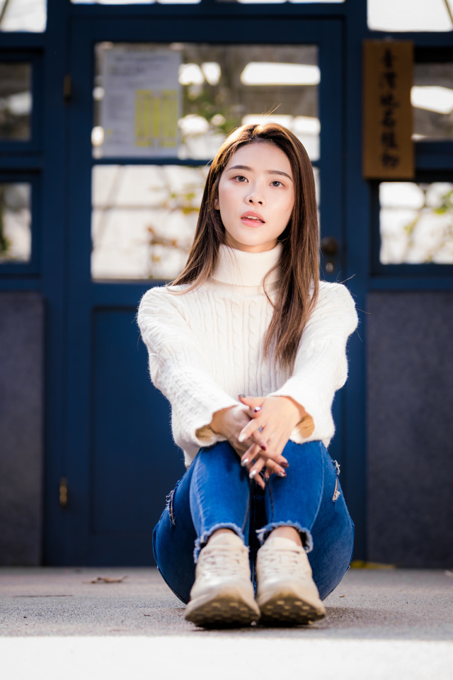 Красивая азиатка в синих джинсах сидит на земле