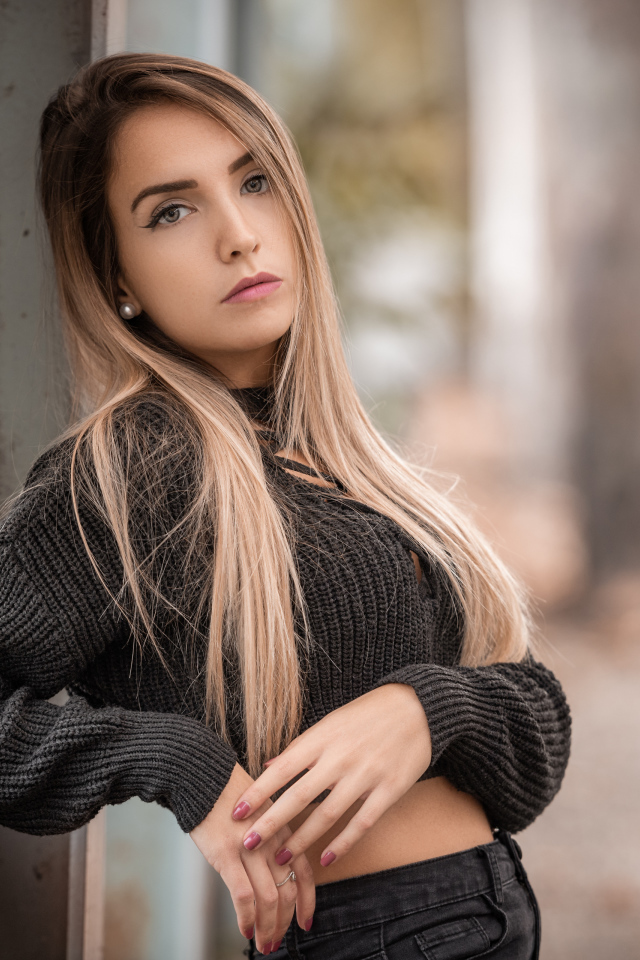 Красивая блондинка в вязаном свитере у стены 