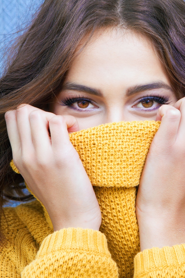 Красивая кареглазая девушка закрывает лицо свитером