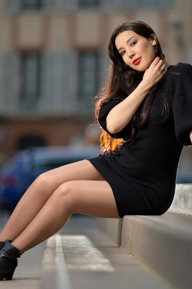 Красивая девушка в черном платье сидит на ступенях