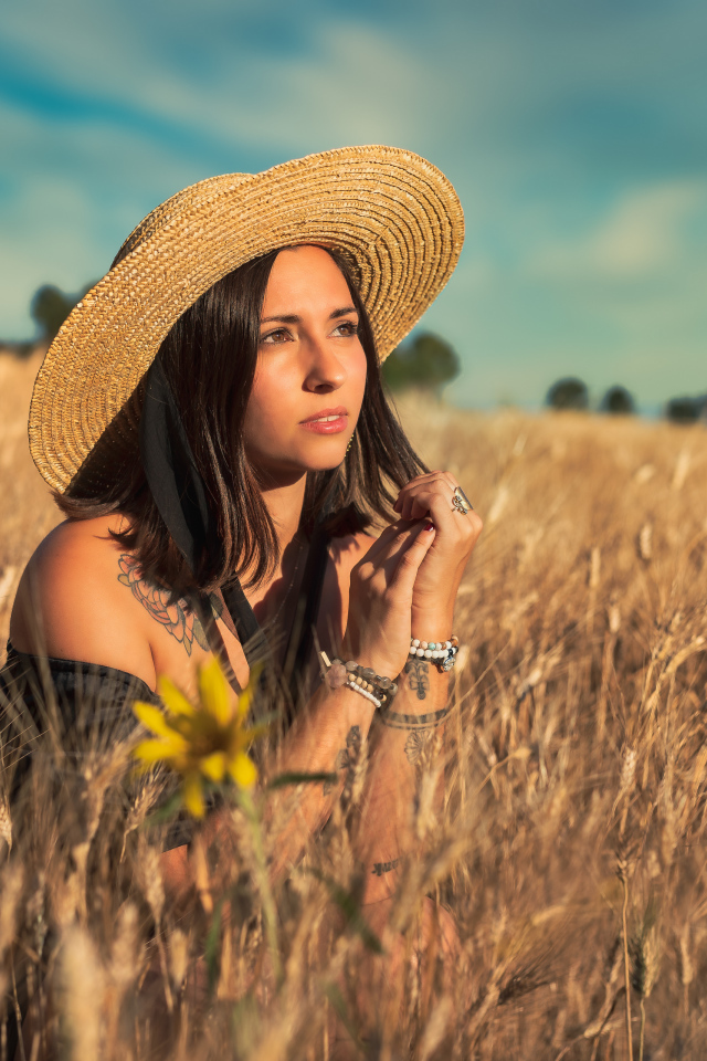 Красивая девушка в шляпе сидит на поле с пшеницей