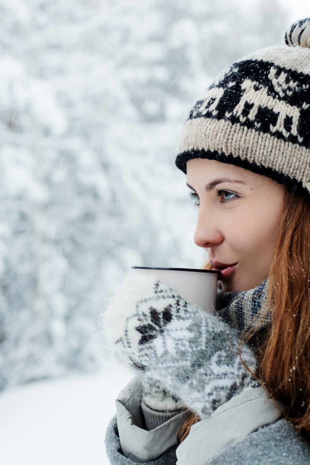 Красивая девушка в теплой шапке пьет кофе зимой на улице 