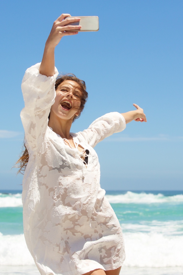 Красивая девушка в белом платье делает селфи на море 