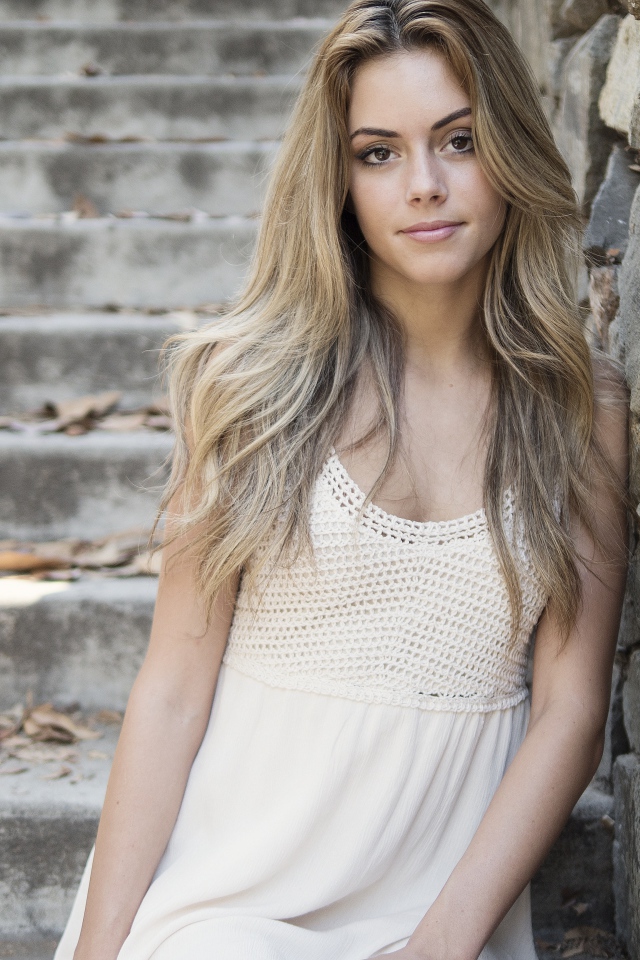 Красивая девушка в белом платье у каменной стены 