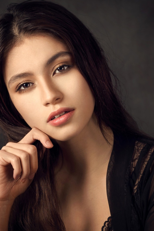 Красивая девушка в черном сидит на сером фоне