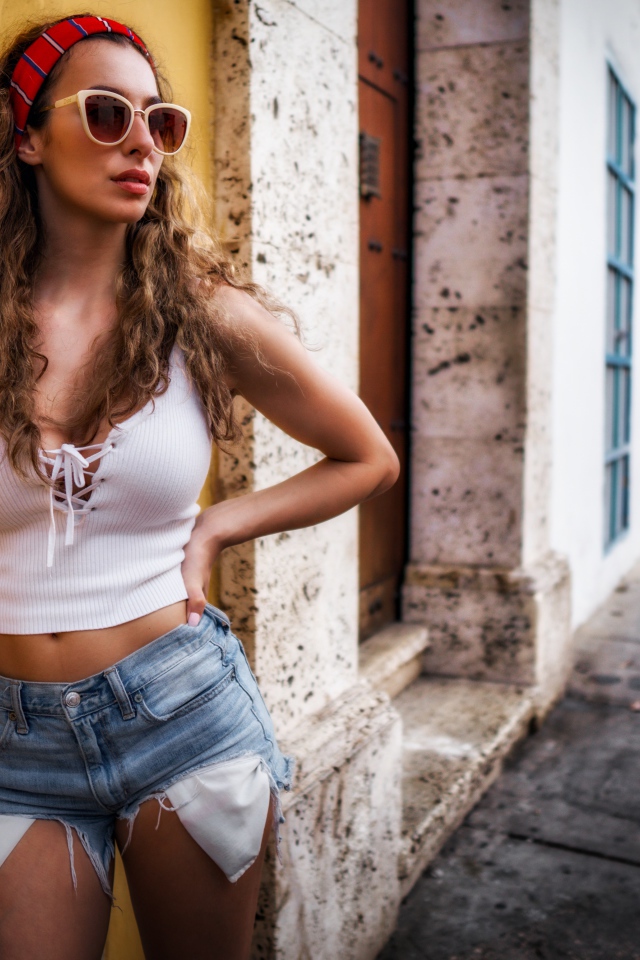 Красивая девушка в солнечных очках стоит у стены