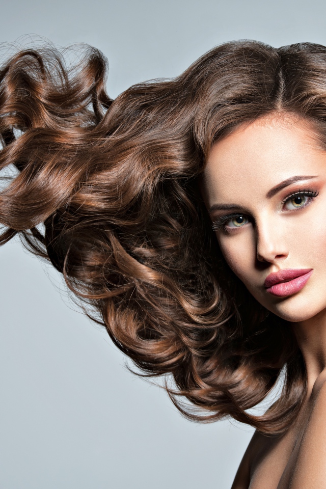 Красивая девушка модель с волнистыми волосами на сером фоне