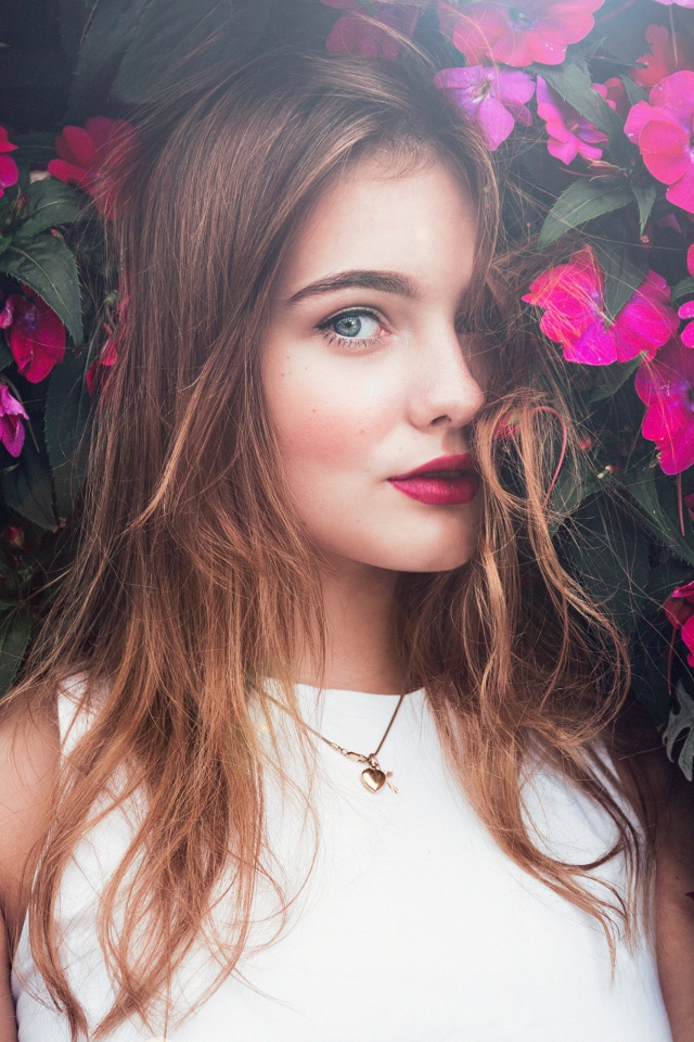 Красивая девушка стоит у зарослей с розовыми цветами