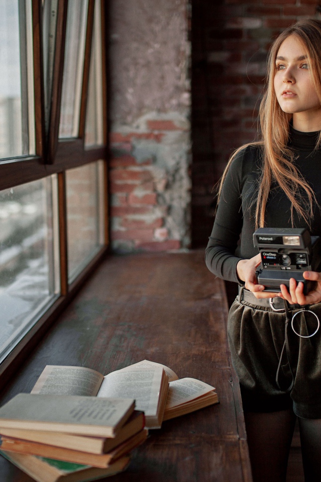 Красивая девушка с фотоаппаратом в руках у окна 