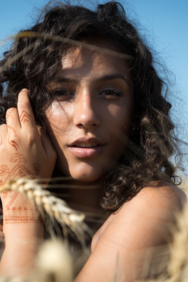 Красивая девушка с рисунком мехенди на руке на пшеничном поле 