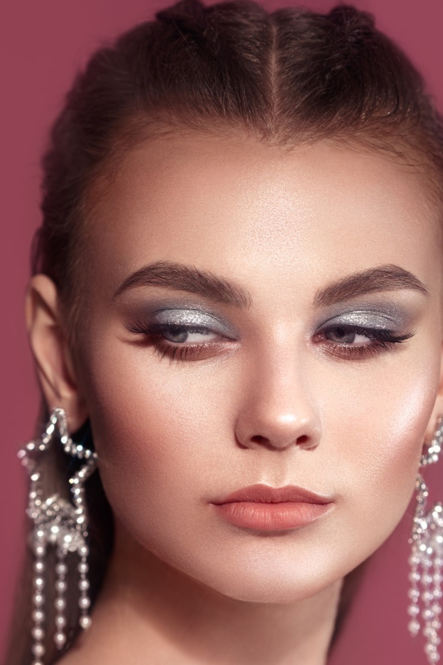 Красивая девушка с макияжем и большими серьгами на розовом фоне