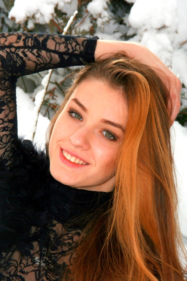 Красивая рыжеволосая девушка у заснеженной туи