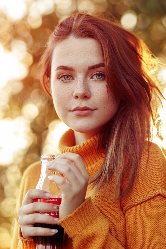 Красивая рыжеволосая девушка с бутылкой кока колы в руке 
