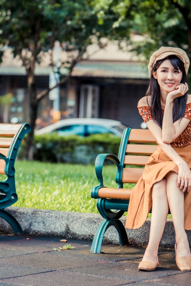 Красивая улыбающаяся азиатка сидит на лавке в парке