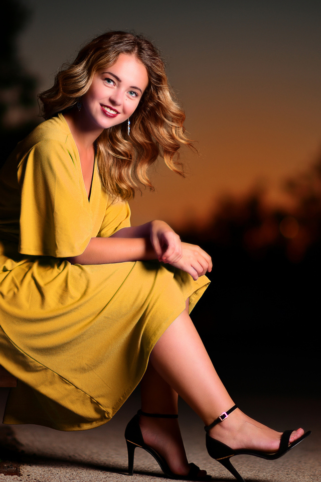 Красивая улыбающаяся девушка в желтом платье сидит на лавке 