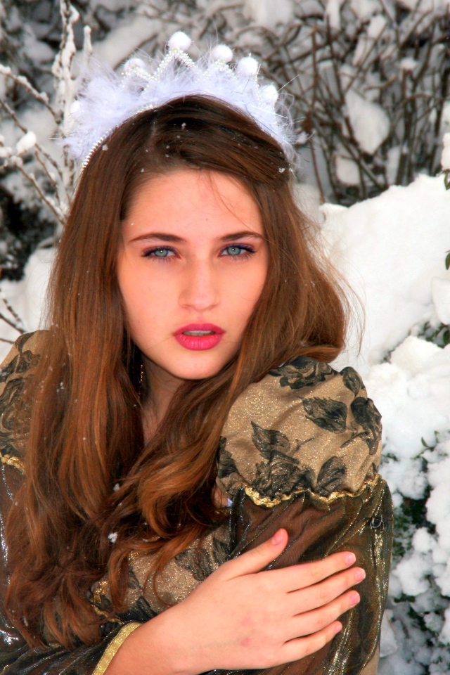 Красивая молодая девушка замерзает у покрытого снегом дерева