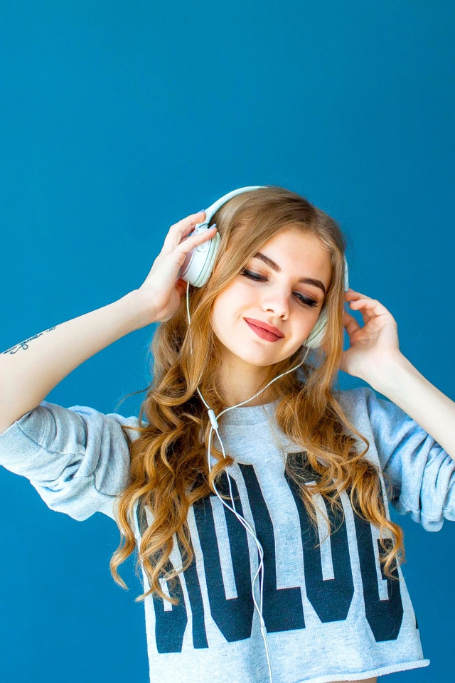 Красивая молодая девушка в наушниках на голубом фоне