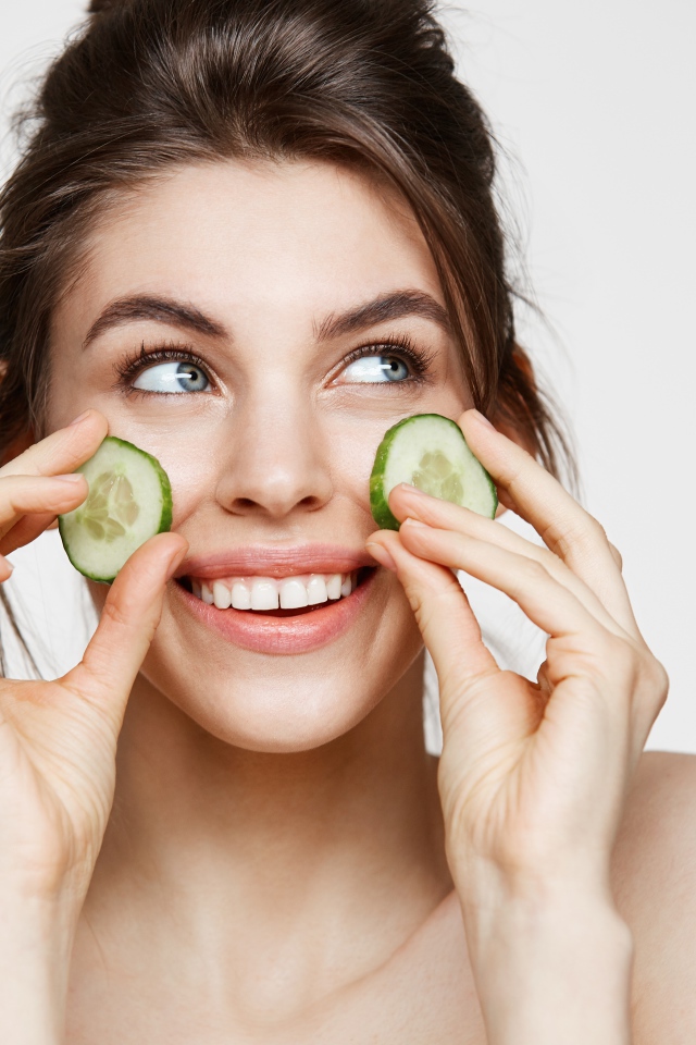 Голубоглазая девушка прикладывает огурцы к лицу 