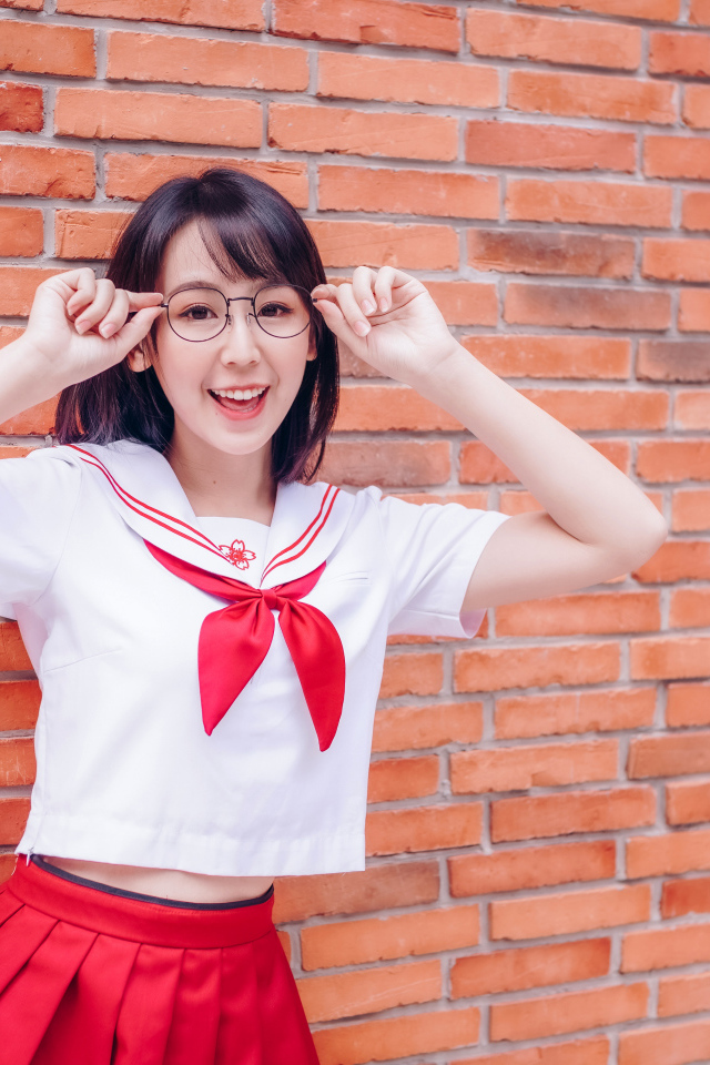 Яркая веселая азиатка в очках у кирпичной стены