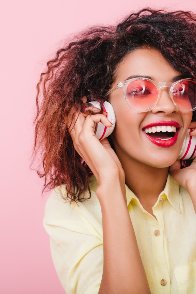 Яркая улыбающаяся девушка слушает музыку в наушниках 