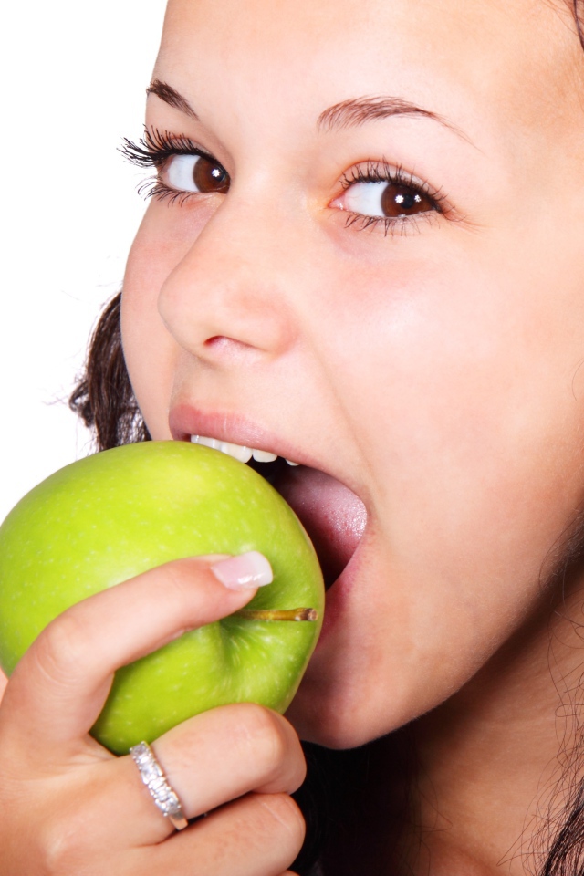 Кареглазая девушка ест зеленое яблоко