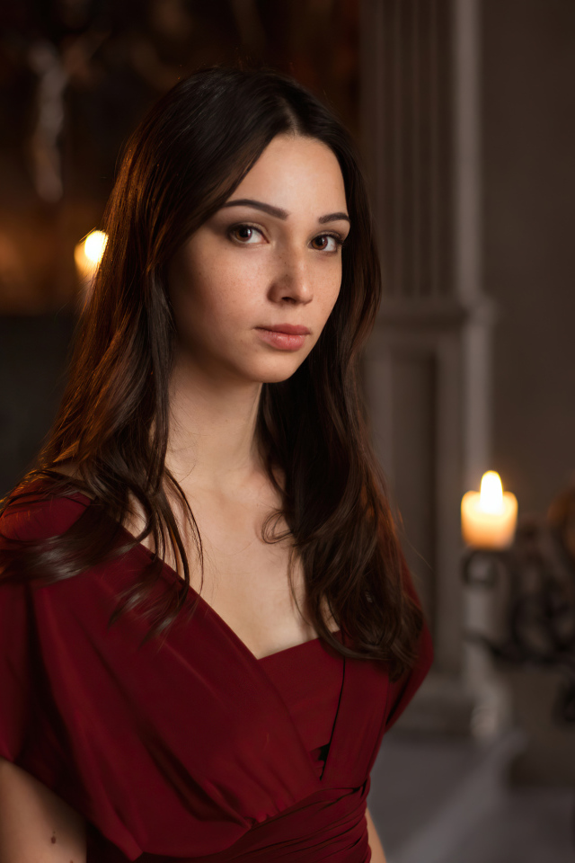 Кареглазая девушка в красном платье в комнате со свечами