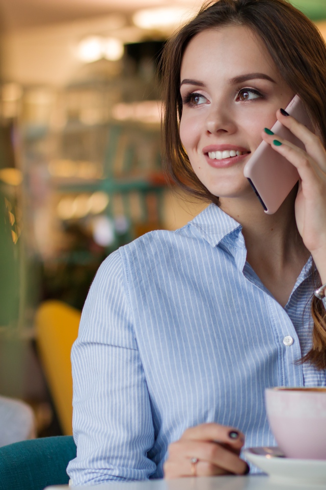 Деловая девушка в рубашке разговаривает в кафе по телефону