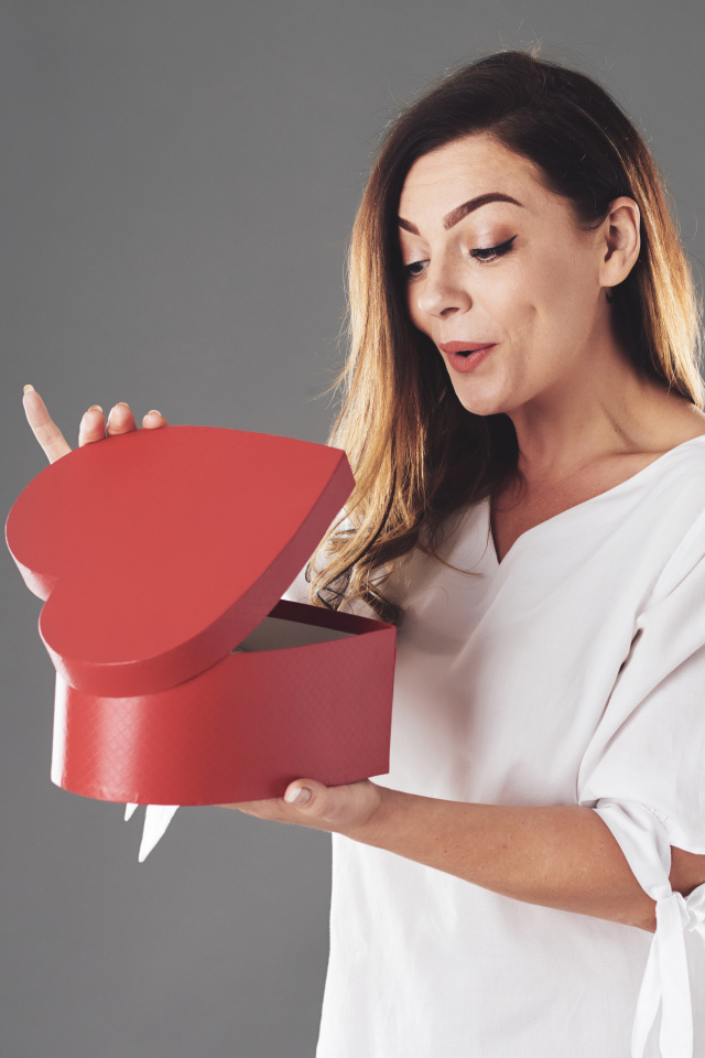 Любопытная девушка смотрит в красную коробку в форме сердца