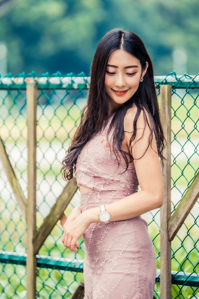 Милая азиатка в платье стоит под забором