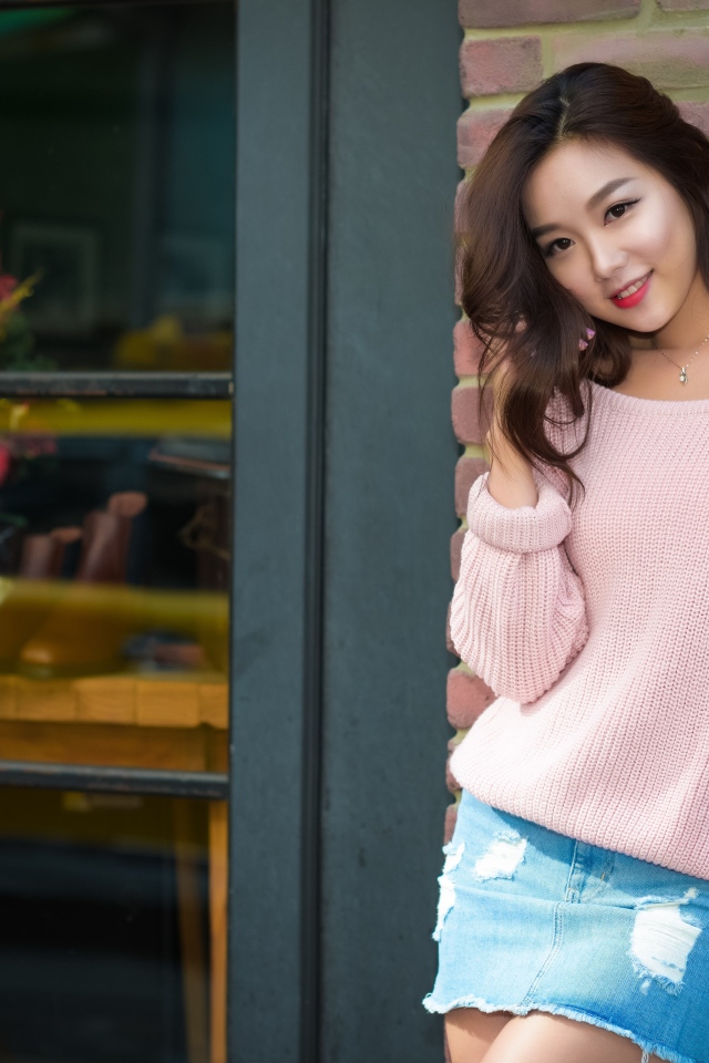 Cute Asian woman in pink sweater stands against the wall