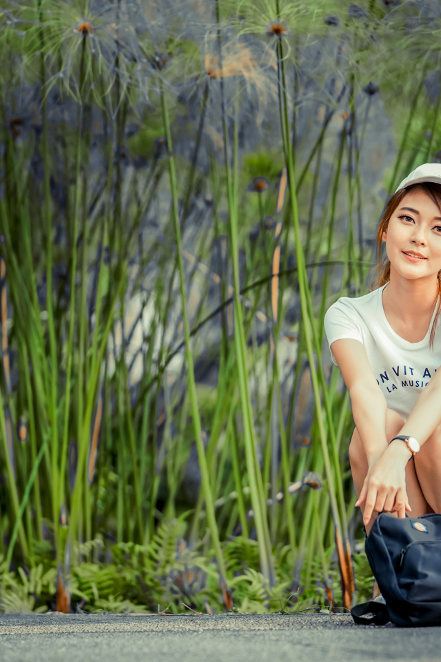 Милая девушка в кепке сидит на дороге с рюкзаком