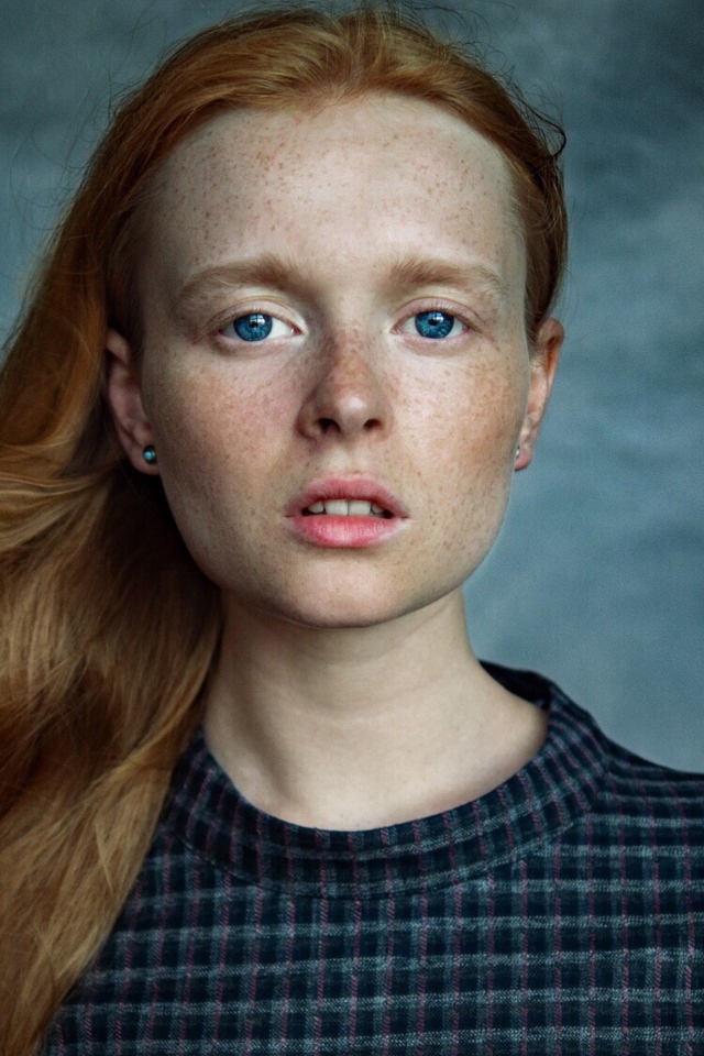 Милая рыжеволосая голубоглазая девушка с веснушками на лице на сером фоне