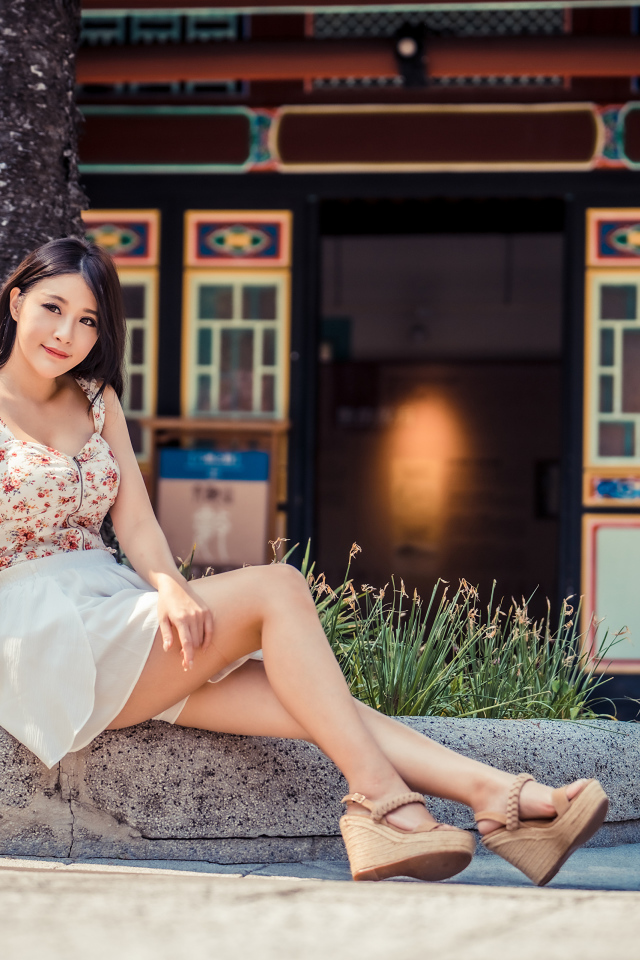 Милая улыбающаяся девушка сидит на бордюре