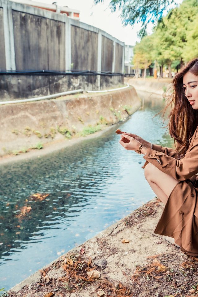 Мечтательная девушка азиатка сидит у воды