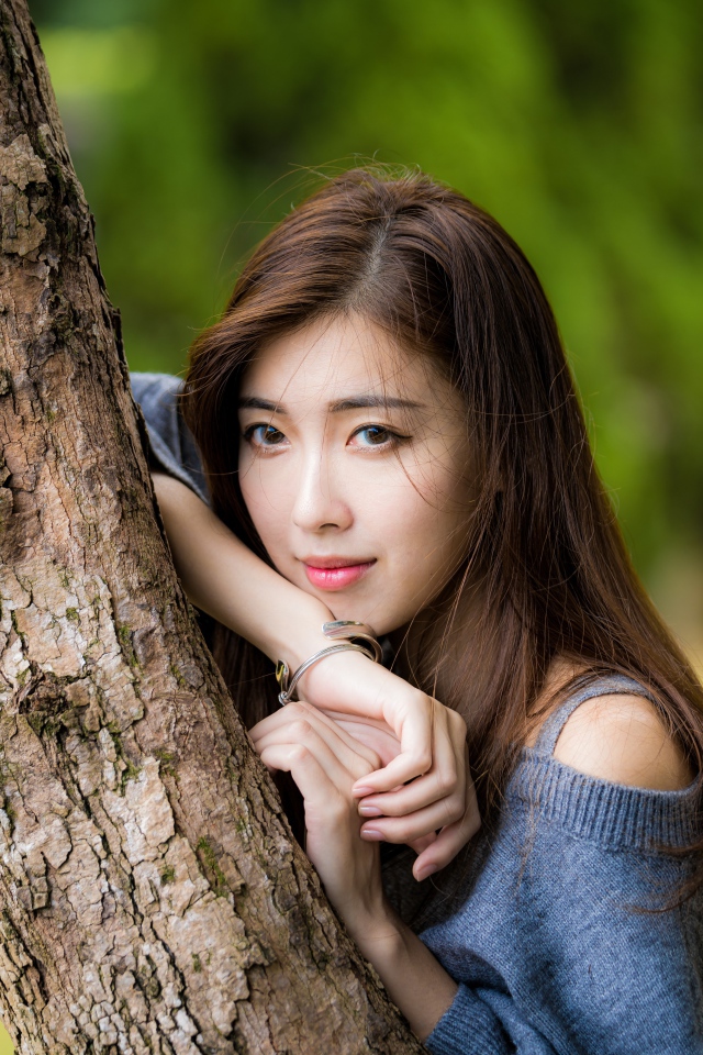 Мечтательная девушка азиатка стоит у дерева