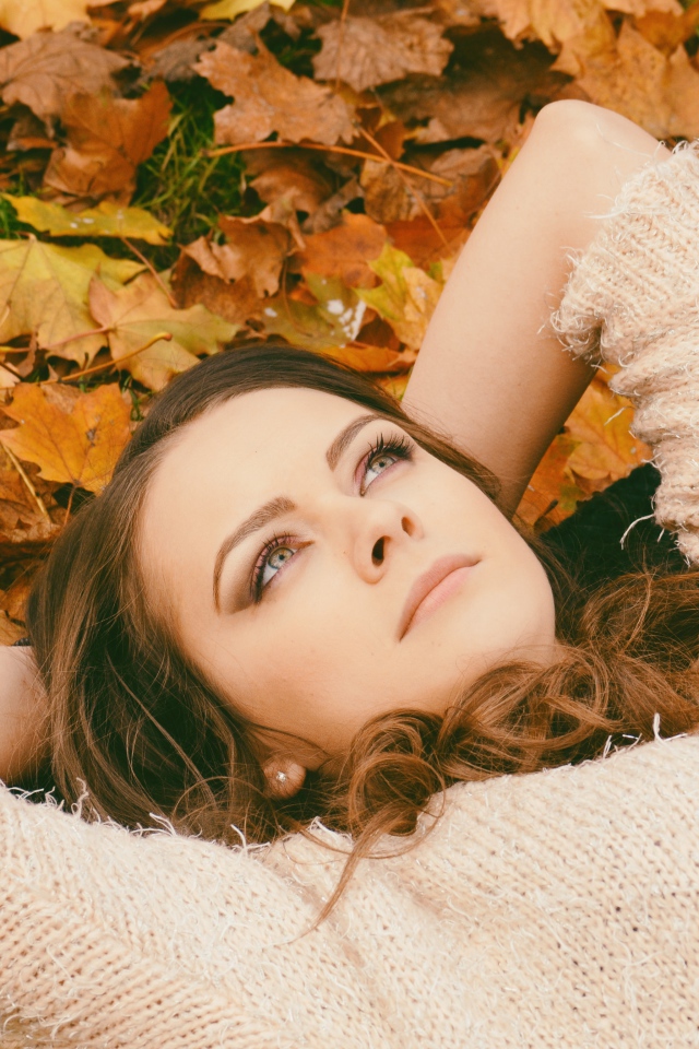 Мечтательная девушка в свитере лежит на земле