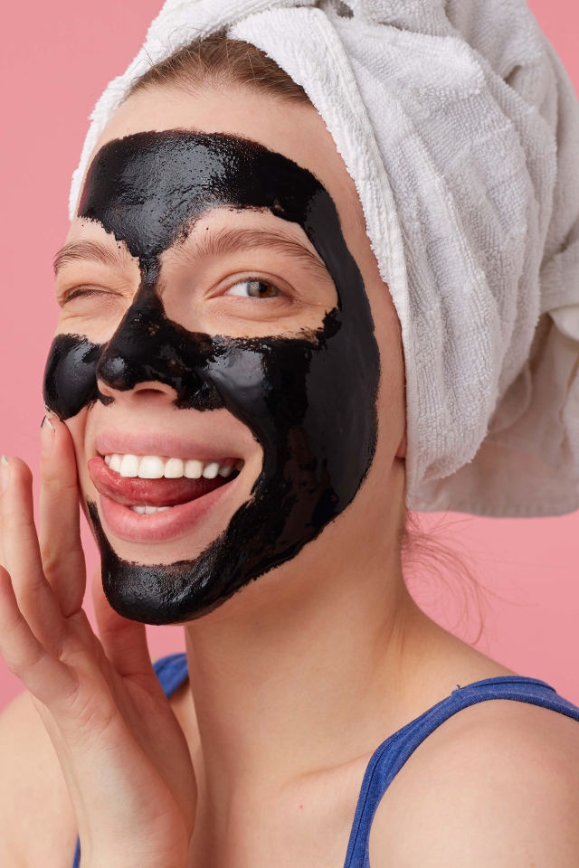 Смешная молодая девушка с черной косметической маской на лице 