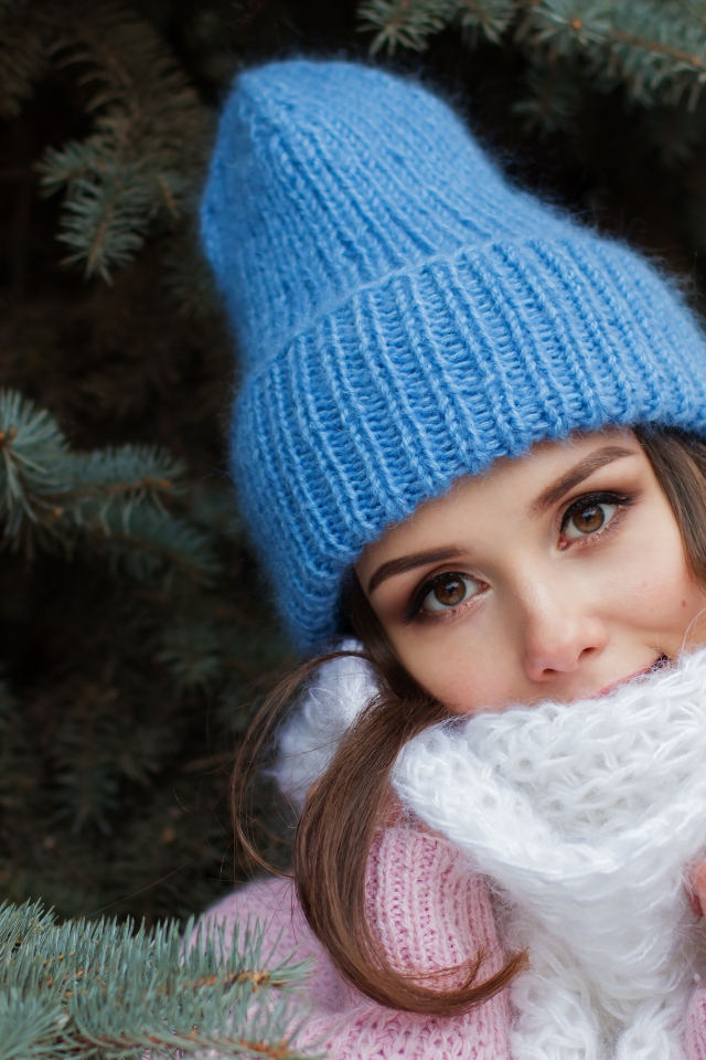 Девушка в голубой вязаной шапке у ели