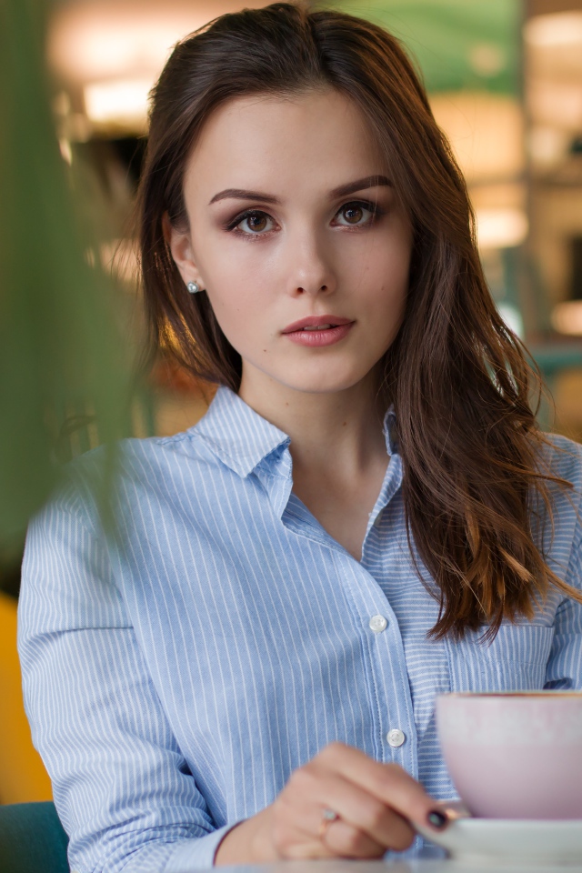 Девушка в голубой рубашке с чашкой кофе на столе в кафе