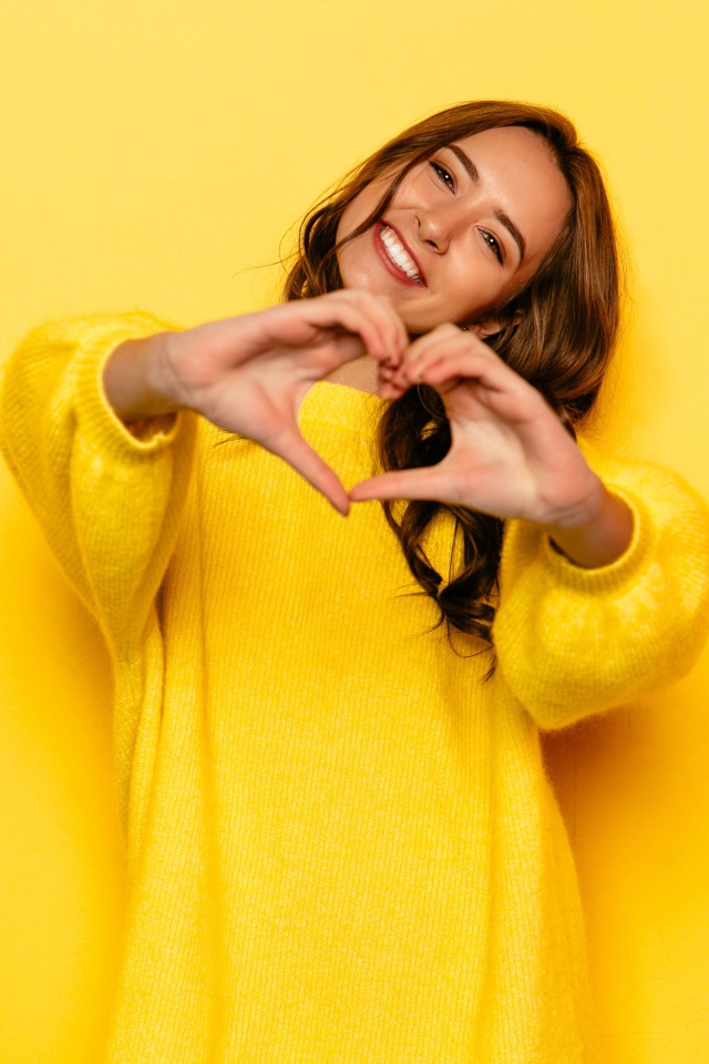 Девушка в желтом свитере показывает сердце руками