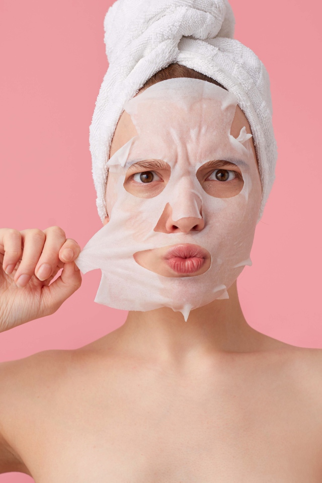 Девушка снимает косметическую маску с лица на розовом фоне 