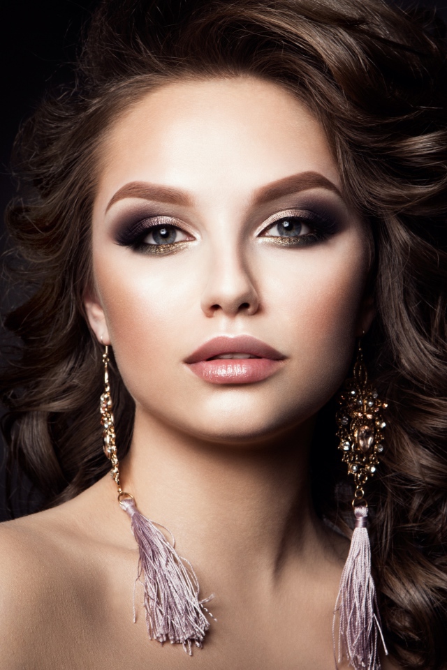 Девушка с прической с красивыми сережками на сером фоне 