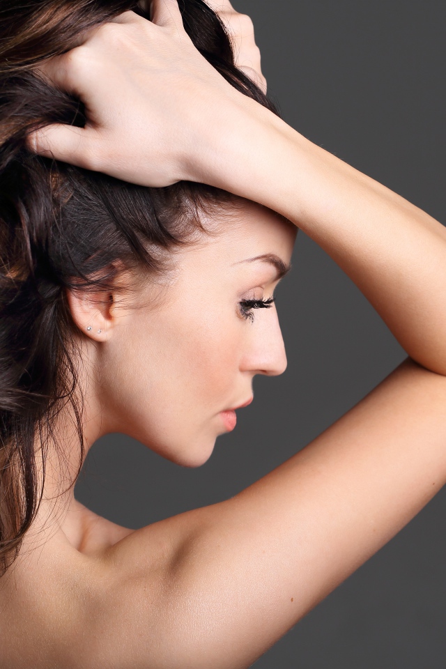 Девушка с руками в волосах на сером фоне