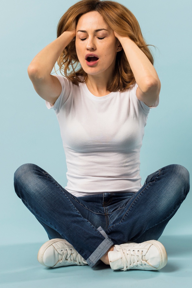 Девушка с руками в волосах сидит в джинсах на голубом фоне