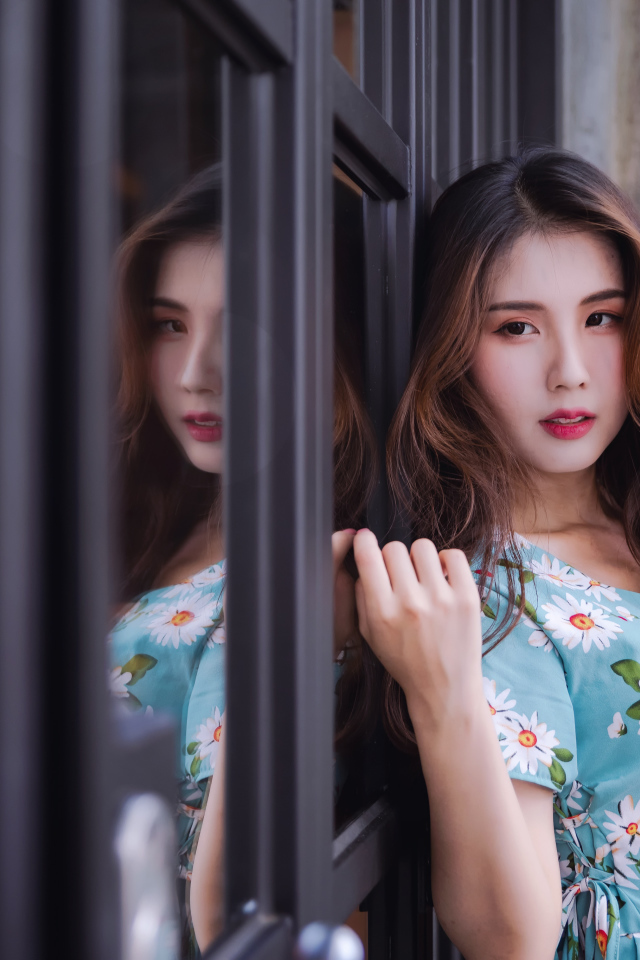 Длинноволосая девушка азиатка стоит у окна