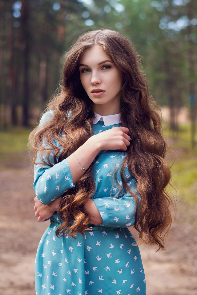 Длинноволосая девушка в голубом платье стоит в лесу