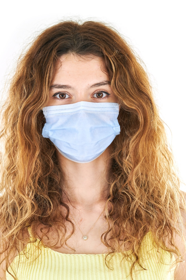 Длинноволосая девушка в маске от коронавируса на белом фоне