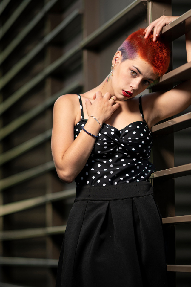 Эпатажная девушка с короткой стрижкой стоит у забора 