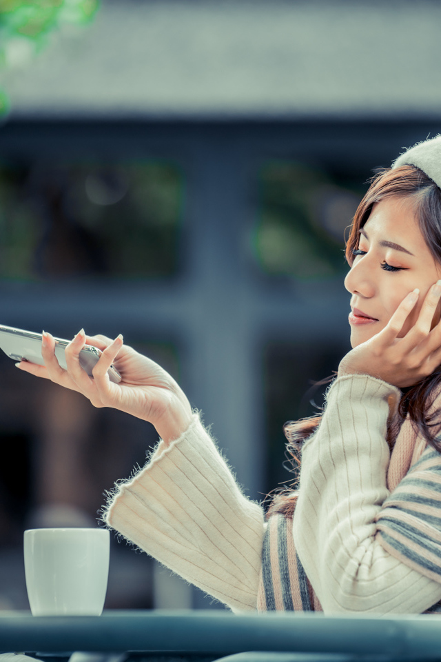 Мечтательная девушка с телефоном сидит в кафе 