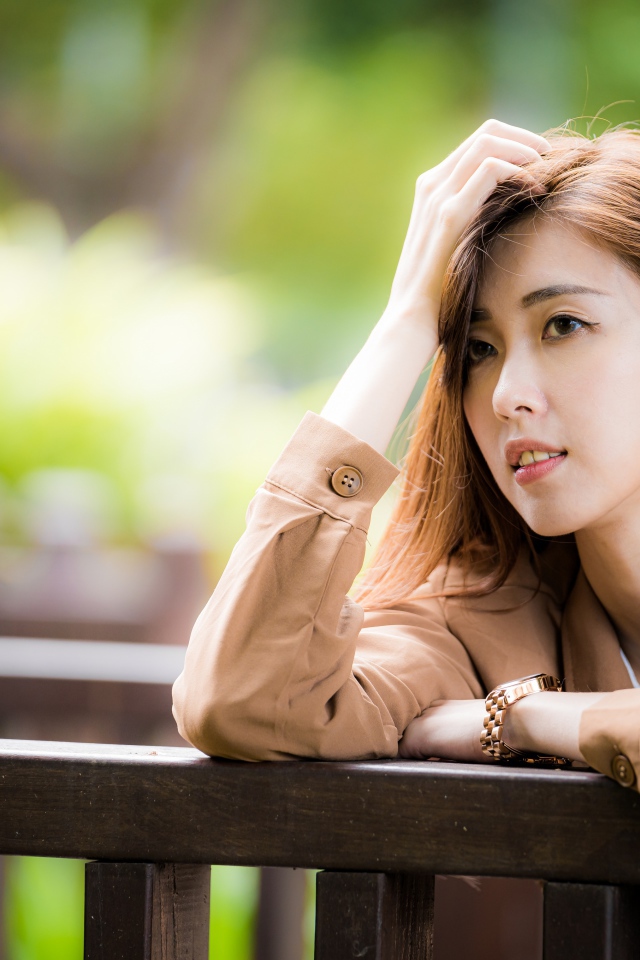 Грустная девушка азиатка стоит у деревянных перил 